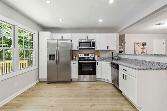 kitchen featuring light wood finished floors, appliances with stainless steel finishes, a sink, and white cabinetry