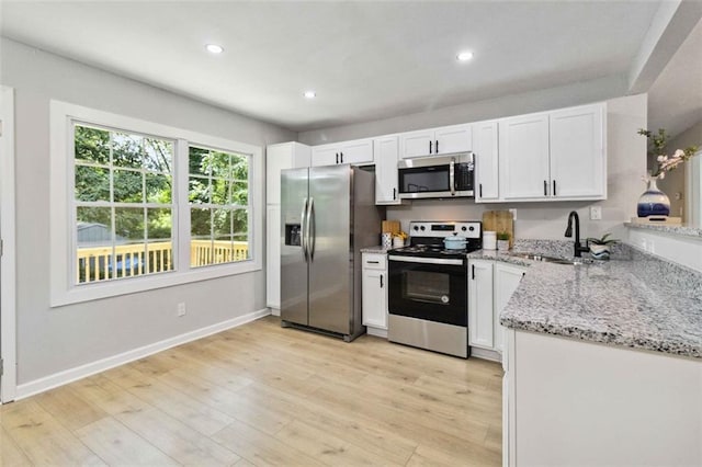 kitchen with light stone countertops, stainless steel appliances, light wood-type flooring, white cabinetry, and a sink