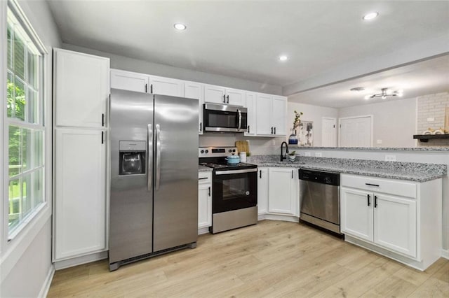 kitchen featuring stainless steel appliances, white cabinets, light wood finished floors, and light stone countertops