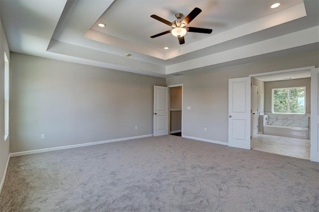 unfurnished bedroom with ensuite bathroom, a raised ceiling, light carpet, and ceiling fan