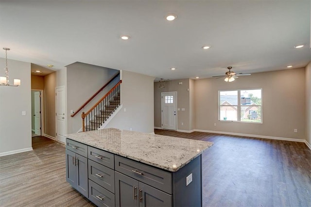 kitchen featuring wood-type flooring, gray cabinetry, hanging light fixtures, a kitchen island, and ceiling fan with notable chandelier