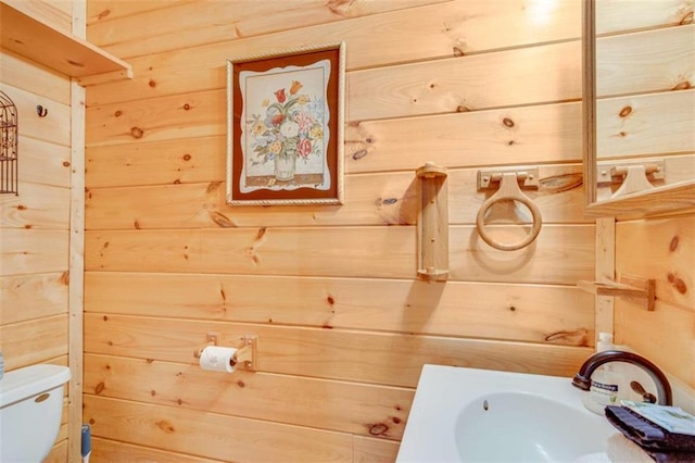 bathroom with toilet, wood walls, and sink