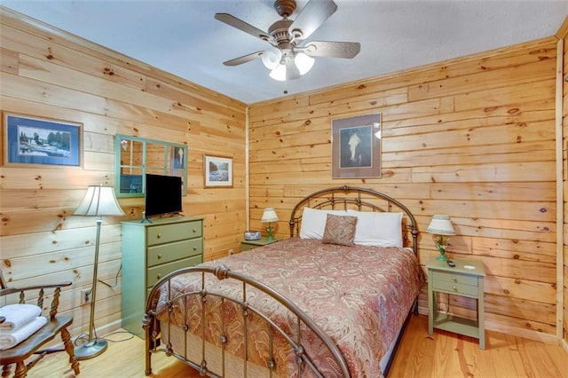 bedroom with ceiling fan, wood walls, and light wood-type flooring