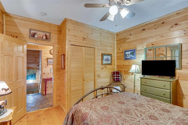 bedroom featuring ceiling fan, wood walls, light wood-type flooring, and a closet