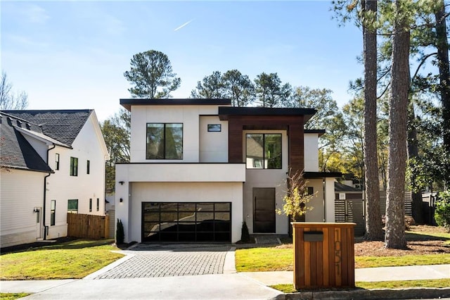 contemporary home with an attached garage, fence, decorative driveway, a front lawn, and stucco siding