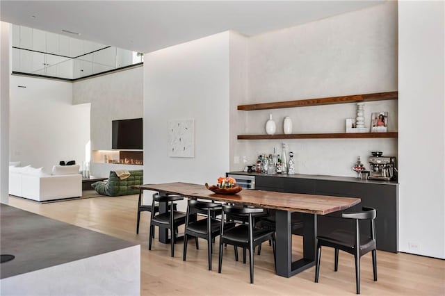 dining space with a bar, a high ceiling, and light wood-style flooring