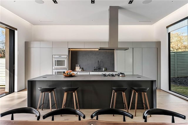 kitchen featuring tasteful backsplash, island range hood, modern cabinets, a breakfast bar area, and gray cabinetry