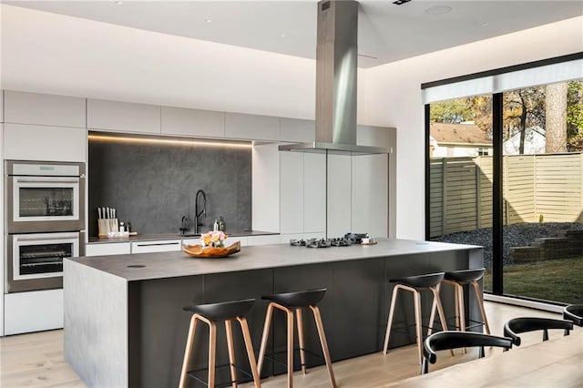 kitchen featuring tasteful backsplash, a large island, modern cabinets, island exhaust hood, and double oven