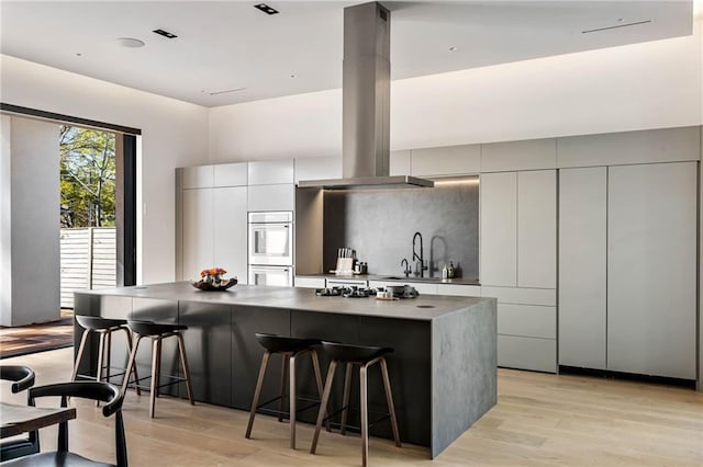 kitchen with island range hood, a large island, modern cabinets, light wood-style floors, and a kitchen bar