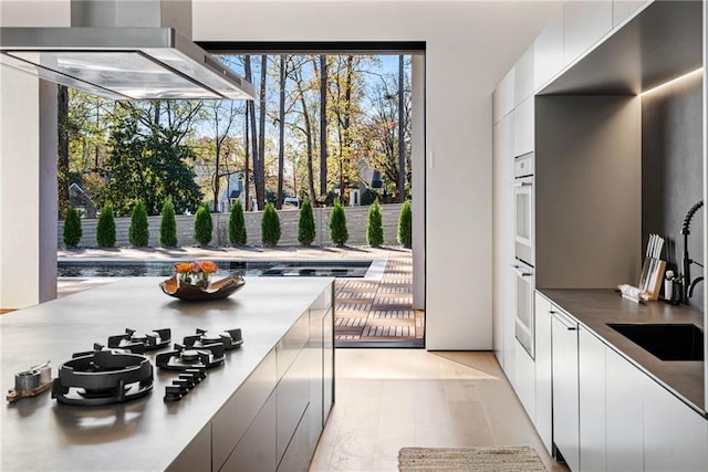 kitchen featuring wall chimney range hood, modern cabinets, white cabinets, and a sink