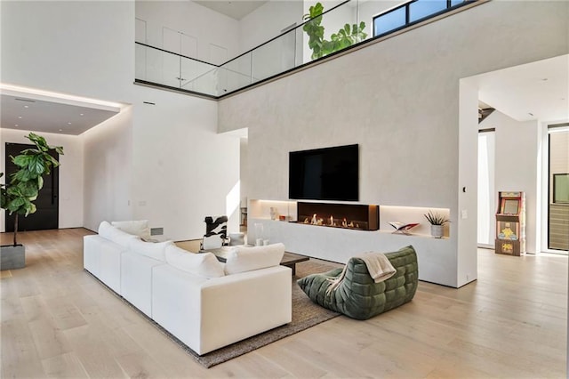 living area featuring a towering ceiling, a warm lit fireplace, and wood finished floors