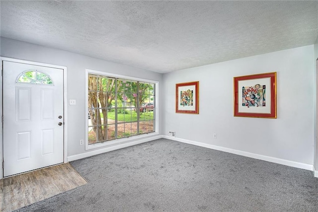 carpeted entryway featuring a textured ceiling, visible vents, and baseboards