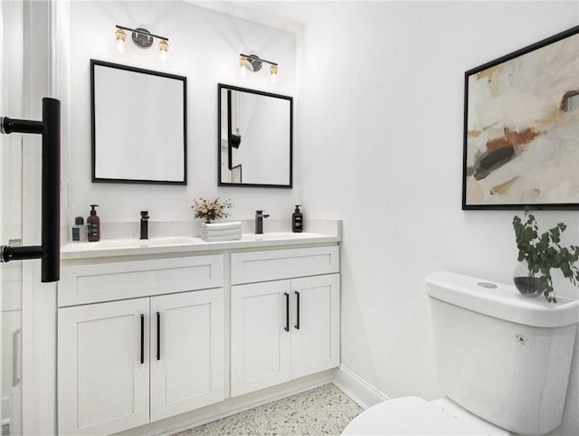 bathroom with a sink, speckled floor, toilet, and double vanity