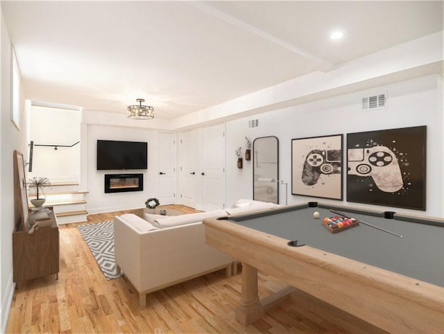 game room with visible vents, a notable chandelier, a glass covered fireplace, and light wood finished floors