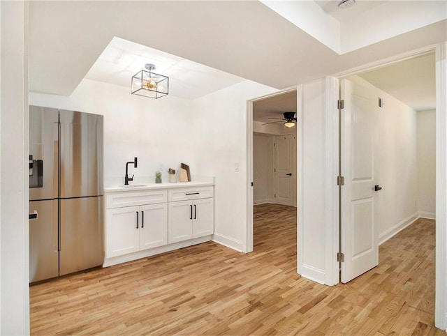 kitchen with light wood finished floors, stainless steel fridge with ice dispenser, a sink, light countertops, and white cabinets