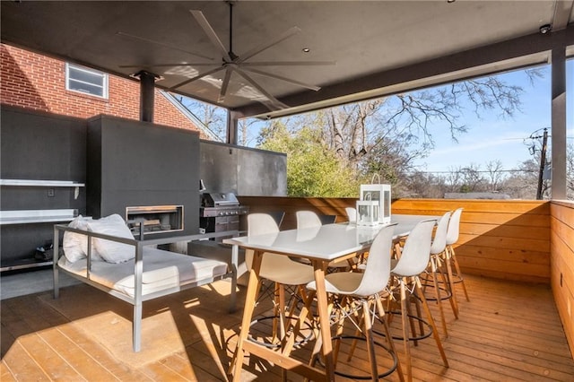 deck with ceiling fan, an outdoor fireplace, a bar, and area for grilling