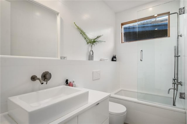 full bathroom with sink, shower / bath combination with glass door, tile walls, decorative backsplash, and toilet