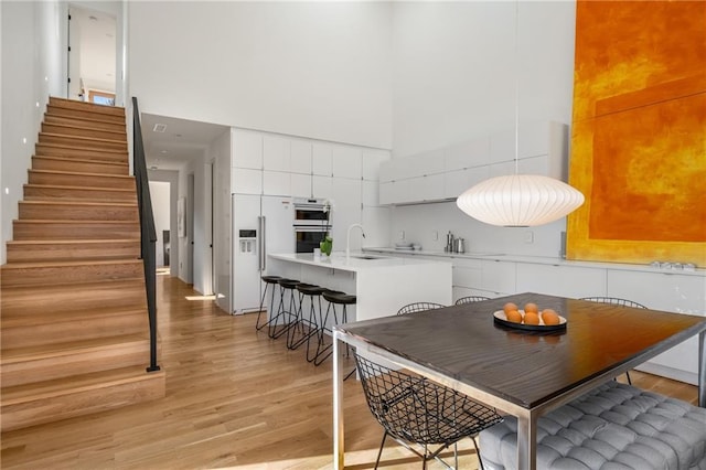 kitchen with sink, built in refrigerator, double oven, a towering ceiling, and white cabinets