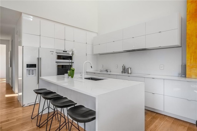 kitchen with sink, white appliances, a kitchen breakfast bar, an island with sink, and white cabinets