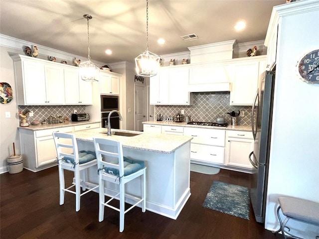 kitchen featuring pendant lighting, light stone counters, an island with sink, sink, and white cabinets