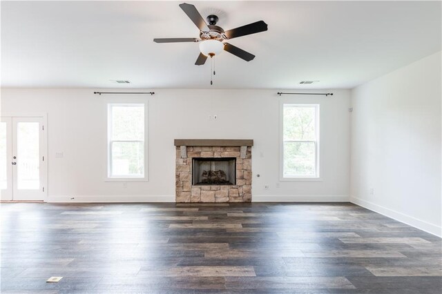 unfurnished living room featuring a wealth of natural light, ceiling fan, dark hardwood / wood-style floors, and a stone fireplace