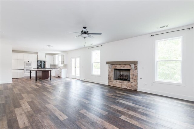 unfurnished living room with a healthy amount of sunlight, a stone fireplace, dark hardwood / wood-style floors, and ceiling fan