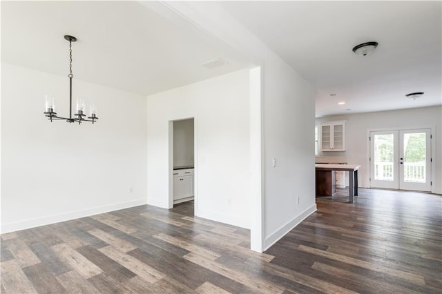 unfurnished room featuring an inviting chandelier, dark hardwood / wood-style floors, and french doors