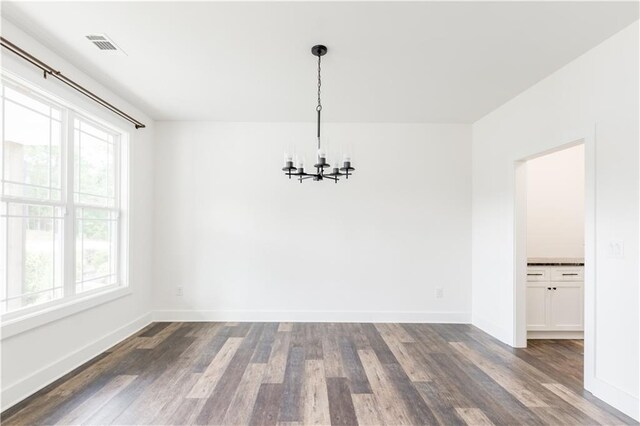 unfurnished dining area featuring a chandelier, plenty of natural light, and dark wood-type flooring