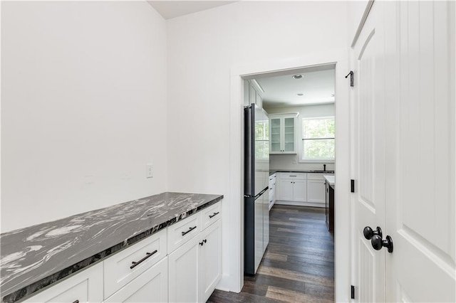 kitchen featuring dark hardwood / wood-style flooring, dark stone countertops, white cabinets, and stainless steel refrigerator