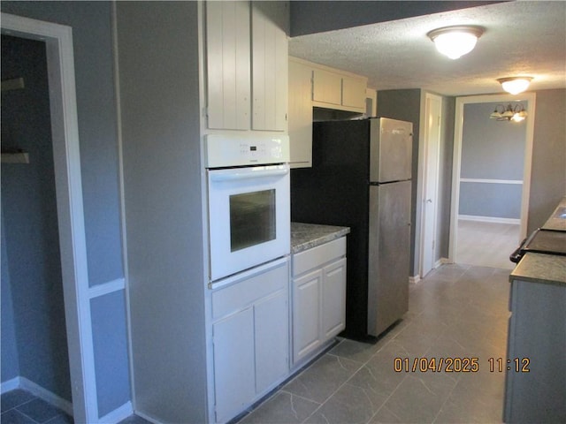 kitchen with a textured ceiling, white oven, white cabinetry, and stainless steel refrigerator