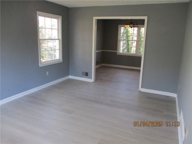 unfurnished room with plenty of natural light, a chandelier, and light hardwood / wood-style floors