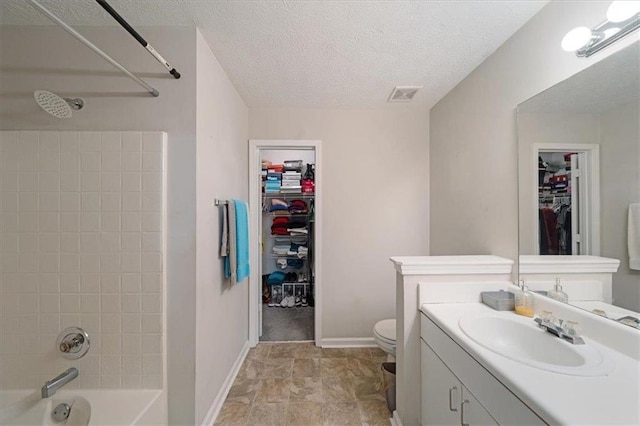 full bathroom with tiled shower / bath, vanity, a textured ceiling, and toilet