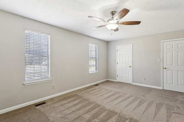 carpeted empty room with a ceiling fan, visible vents, and baseboards