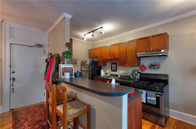 kitchen with light hardwood / wood-style floors, black fridge, a breakfast bar area, gas range, and crown molding