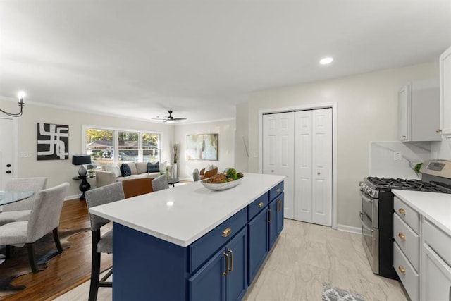 kitchen featuring gas stove, blue cabinetry, a breakfast bar, white cabinets, and ceiling fan with notable chandelier