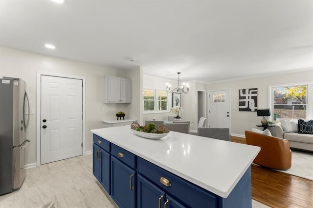 kitchen with stainless steel refrigerator, a center island, an inviting chandelier, blue cabinets, and pendant lighting