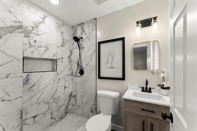 bathroom with tiled shower, vanity, and toilet