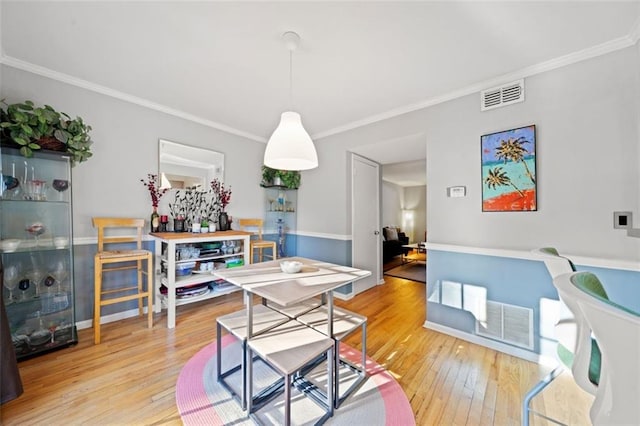 dining area featuring baseboards, visible vents, wood-type flooring, and ornamental molding