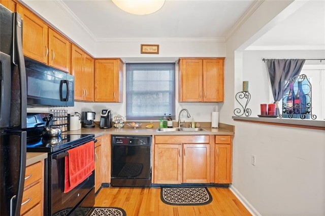 kitchen featuring light countertops, ornamental molding, light wood-style flooring, black appliances, and a sink