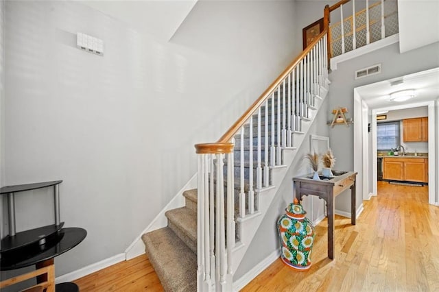 staircase featuring visible vents, a high ceiling, baseboards, and wood finished floors