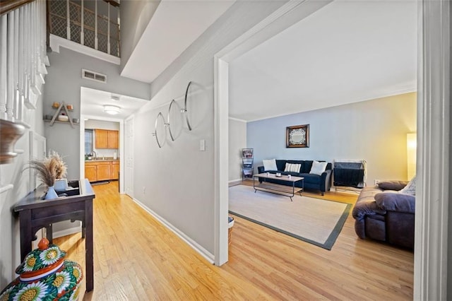 hall with light wood finished floors, visible vents, baseboards, and a sink