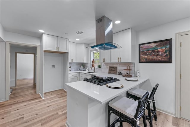 kitchen featuring island range hood, a sink, a peninsula, light countertops, and white cabinets
