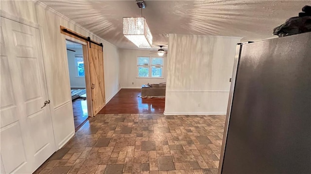 hallway with ornamental molding, stone finish flooring, a barn door, and baseboards