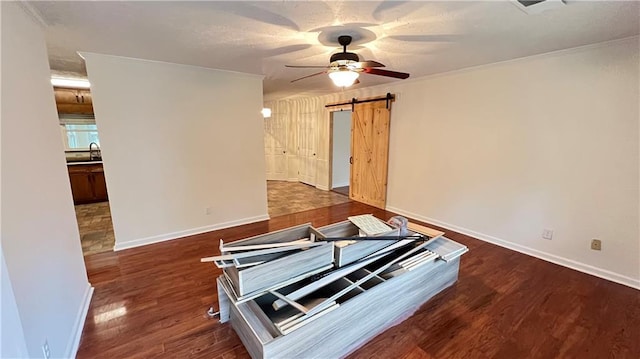 interior space featuring a barn door, ornamental molding, ceiling fan, wood finished floors, and baseboards