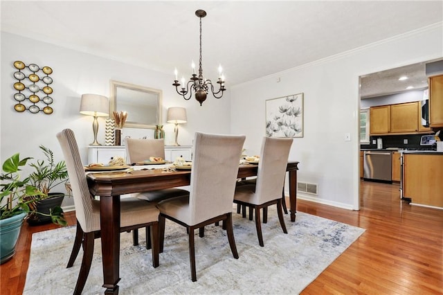 dining room featuring visible vents, baseboards, a notable chandelier, light wood-style floors, and ornamental molding