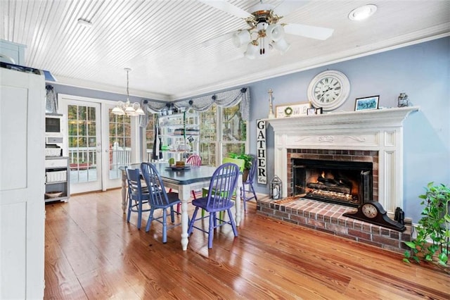 dining area featuring ceiling fan, a fireplace, crown molding, and hardwood / wood-style flooring