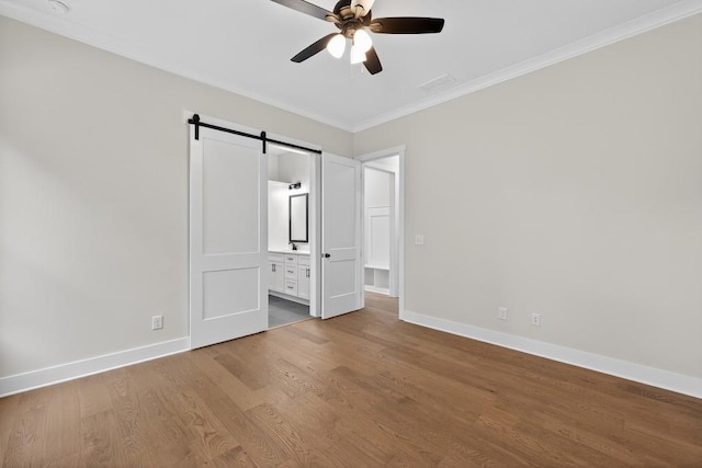 305 Milledge Ave, Monroe, GA 30655 - unfurnished bedroom with crown molding, a barn door, wood finished floors, connected bathroom, and a ceiling fan