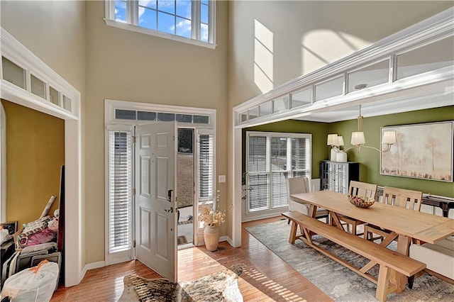 entryway featuring light wood-type flooring, a towering ceiling, and baseboards