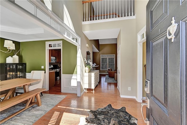 foyer featuring wainscoting, crown molding, light wood-style flooring, and a high ceiling