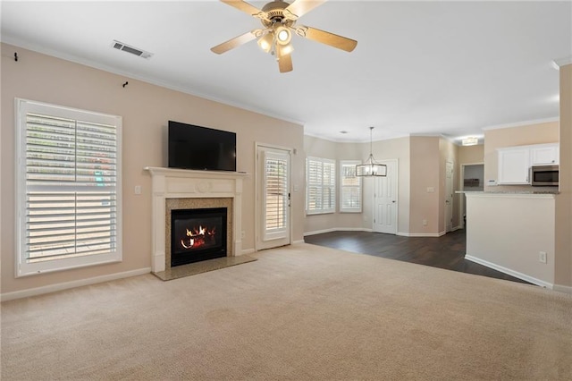 unfurnished living room featuring visible vents, ornamental molding, a ceiling fan, a fireplace, and dark colored carpet